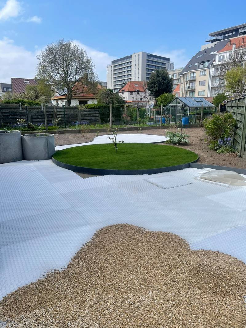Witte grindplaten die worden opgevuld met grind, naast een rond gazon