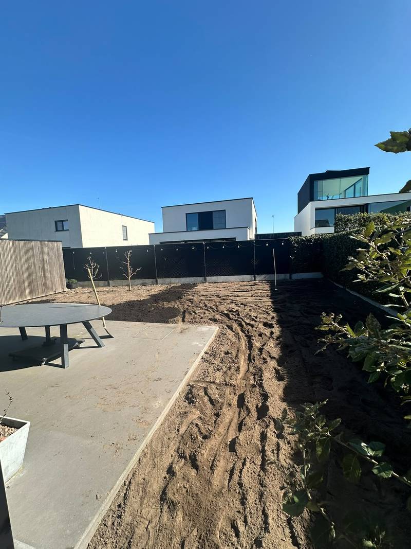 Losgewerkte en uitgevlakte grond naast een betonnen terras, klaar voor de verdere aanleg van de tuin