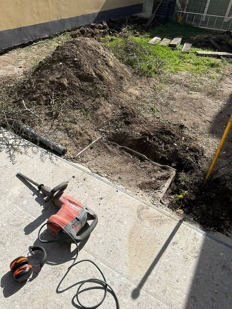 Uitgegraven bodem in een stadstuin, met een breekhamer en gehoorbescherming op het terras