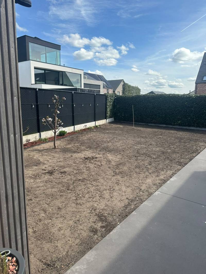 Genivelleerd terrein, klaar voor een nieuw gazon, langs een zwarte omheining en een haag