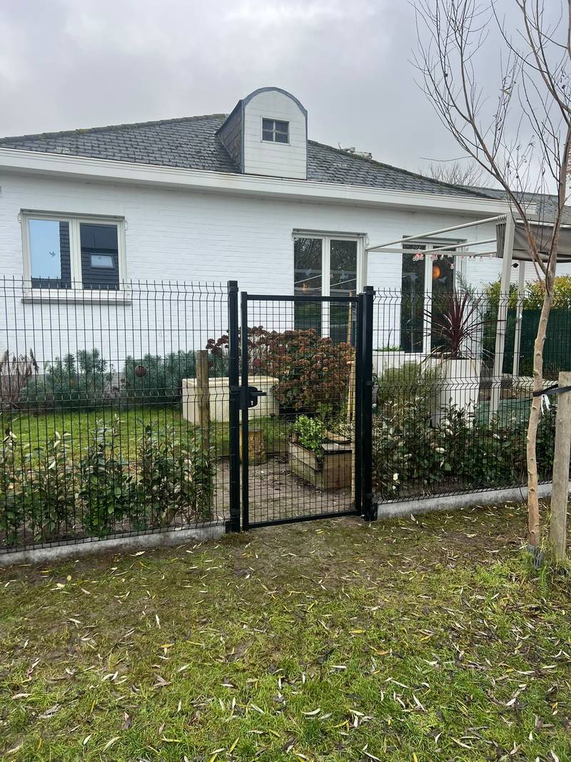 Zwarte tuinpoort in een omheining van draadpanelen met haagplanten erachter
