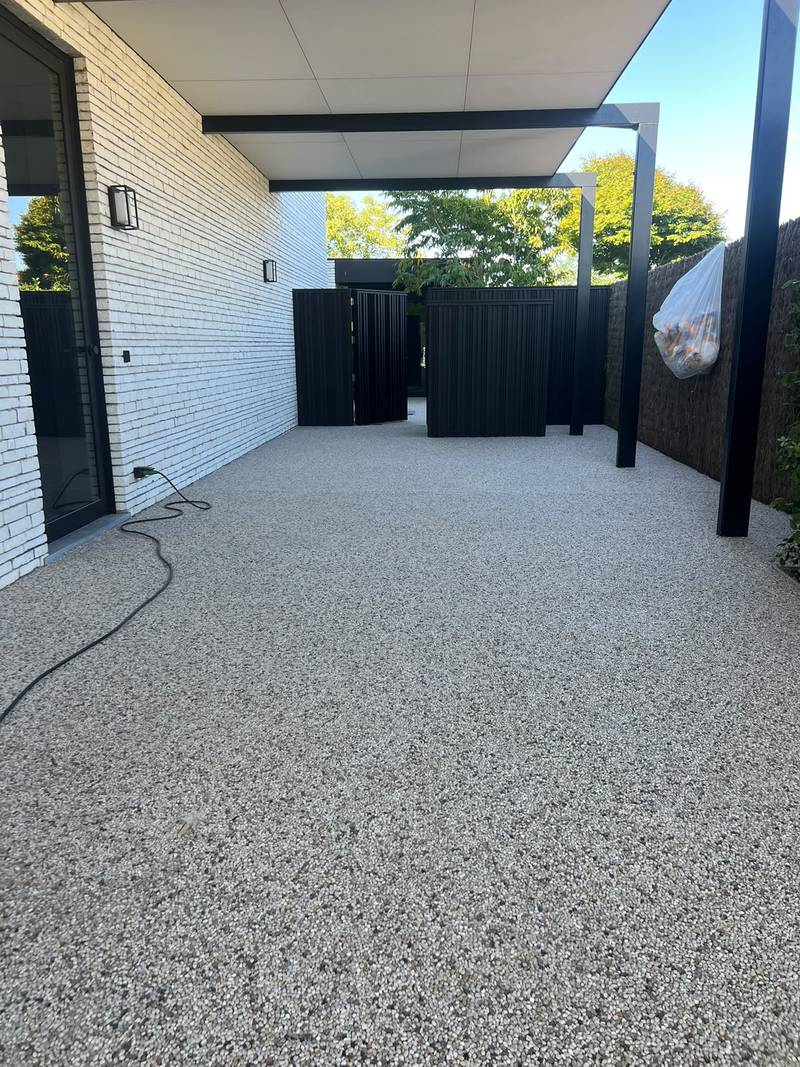 Grindverharding onder een overdekte zone naast een woning met witte gevelsteen
